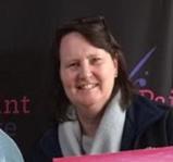 A woman smiling for the camera in front of a pink sign.